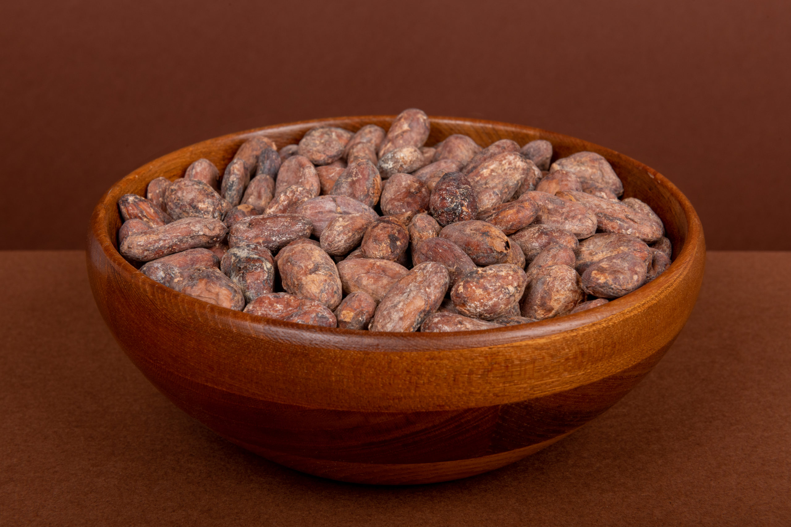 Des fèves de cacao sont rassemblées dans un bol en bois.
