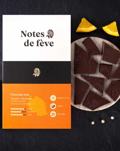 Une tablette de chocolat Bean to bar avec un emballage orange. Autour, du gâteau au vin cuit, de l'orange et du poivre blanc.
