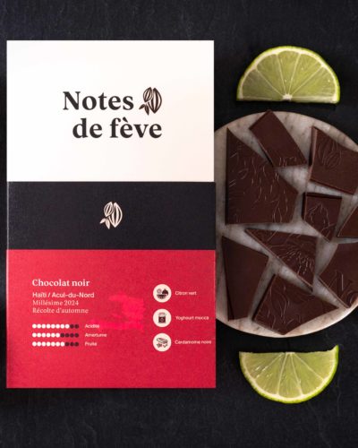 Une tablette de chocolat bean to bar avec un emballage rouge. Autour, du citron vert, du yogourt moccas et de la caradamome