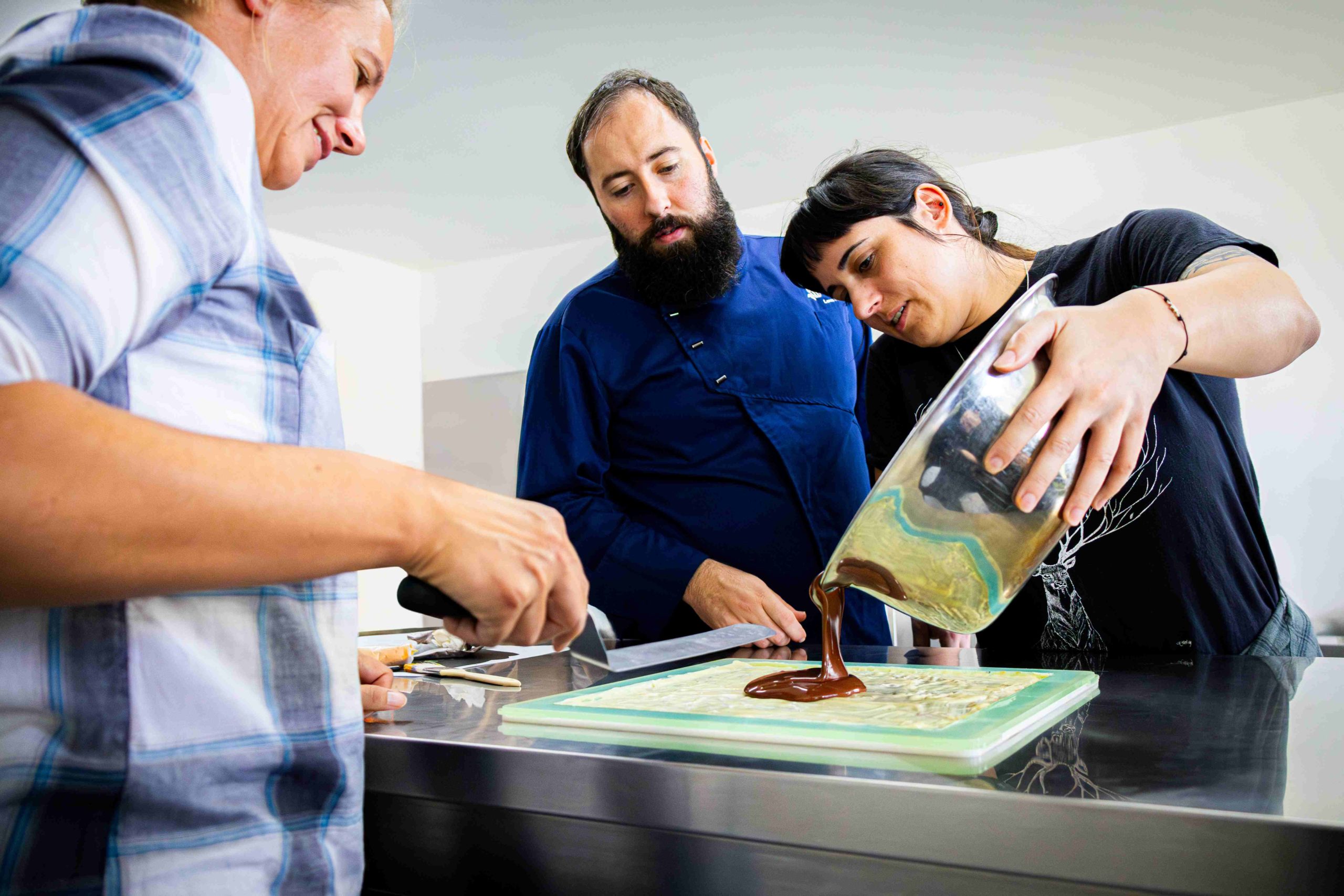 Deux personnes sont en train de confectionner une grande tablette de chocolat, aidées par un chocolatier