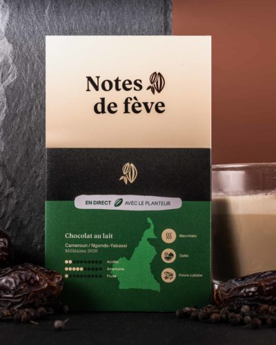 Une tablette de chocolat au lait à l'emballage vert, entourée par des dattes, du poivre, et un verre de Latte Macchiato