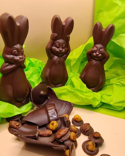 Trois lapins se cachent les yeux, les oreilles et la bouche autour d'un pot en chocolat cassé.